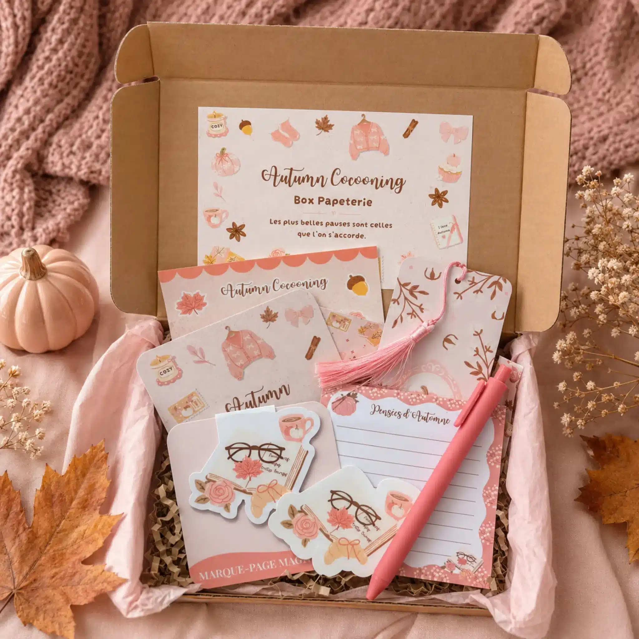 Box papeterie Autumn Cocooning ouverte : carte, planche de stickers, marque-pages, bloc-notes et stylo rose sur papier de soie