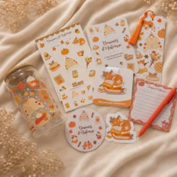 Contenu de la box Réconfort Douceurs d’Automne à plat : gobelet 16 oz, stickers renard, print A5, marque-pages, sous-verre rond, bloc-notes et stylo orange
